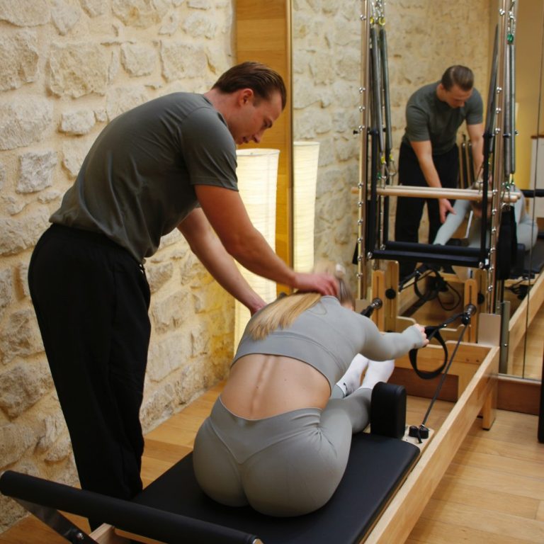 Entrenador asistiendo a una mujer en una sesión de pilates en un estudio.