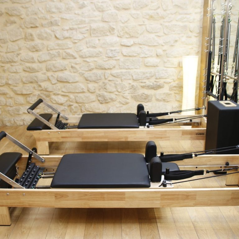 Máquina de reformer pilates de madera con almohadillas negras en un espacio luminoso.