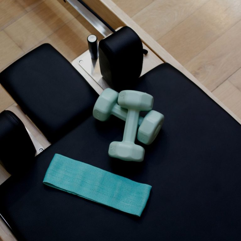 Un par de pesas de color claro y una toalla en un banco de ejercicios. Pilates reformer