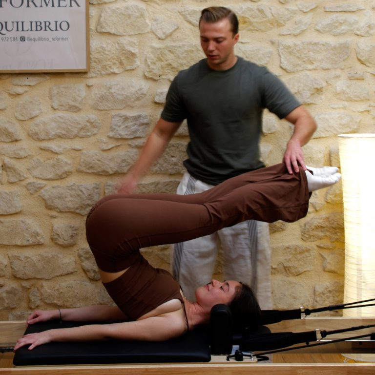 Una mujer realiza un ejercicio de pilates con la ayuda de un instructor.